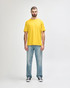 A man wearing a bright yellow Gildan Softstyle adult T-shirt and grey jeans, standing casually.