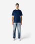 A model wearing a navy blue Gildan Softstyle T-shirt paired with light blue jeans. The T-shirt has a logo on it.
