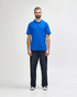 A model wears a blue Gildan Softstyle Adult Double Pique Polo with short sleeves, paired with light blue jeans.