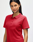 A woman is wearing a red Gildan Softstyle ladies' double pique polo, featuring a classic collar and buttons.