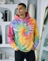 A hoodie in vibrant tie-dye colours of pink, yellow, green, and purple, worn by a young man. It has a front pocket and hood.
