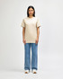 A light khaki midweight t-shirt is worn by a model paired with black pants and sneakers, also featuring a logo.