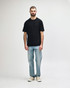 A black midweight t-shirt displayed on a model, paired with black jeans and sneakers. Features a logo.