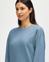 A blue Gildan Softstyle adult sweatshirt is worn by a model adjusting their sleeves, featuring a logo on the garment.