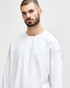 A white Gildan Softstyle adult sweatshirt is worn by a model with dark hair, featuring a relaxed fit and long sleeves.
