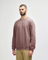 A softstyle adult sweatshirt in a mauve colour, featuring long sleeves and a relaxed fit. It has a logo.