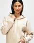 A model wearing a beige Gildan Softstyle adult hooded sweatshirt with the hoodie drawn over her head.