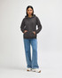A woman wears a grey hooded sweatshirt with a logo, paired with denim jeans and white sneakers.