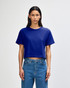 A blue women's boxy T-shirt with short sleeves, featuring a logo on the fabric, styled with light jeans.