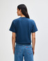 A navy blue women's boxy T-shirt featuring a loose fit, viewed from the back. The model wears light blue cargo pants.