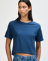 A navy blue boxy t-shirt with short sleeves, displayed on a model with curly hair. The shirt has a logo.