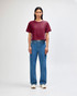 A woman stands wearing a burgundy boxy T-shirt and light blue cargo jeans, paired with black and white sneakers.