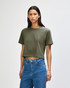 A woman wears an olive green boxy t-shirt, styled with light blue jeans, against a plain background.