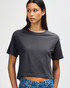 A woman models a grey boxy T-shirt with short sleeves and a relaxed fit, paired with light denim jeans.