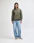 A model wearing an olive green unisex hooded sweatshirt, paired with black cargo pants and sneakers.
