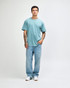 A man wearing a light blue unisex short sleeve t-shirt with denim jeans, standing against a plain background.