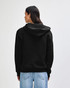 A model wearing a black unisex full zip hooded sweatshirt paired with light blue baggy jeans and black sneakers.