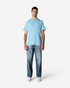 A man wearing a light blue Gildan Light Cotton T-shirt paired with faded jeans and white shoes, standing against a plain background.