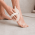 A natural loofah exfoliating shower sponge in beige being used on a foot, showcasing its textured surface.