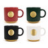 A set of four ceramic coffee mugs in red, green, black, and white, each with a gold medal on the base and a logo.