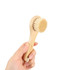 A natural wooden face brush with a light wooden handle and soft bristles, held in a hand.
