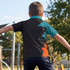 A boy wearing a black, teal, and orange custom youth active polo shirt in an outdoor playground setting.
