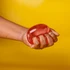 A hand squeezing a translucent red jelly cube sensory toy against a bright yellow background.