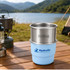 A stainless steel round bottom camping mug sits atop a light blue silicone base, set against a scenic outdoor backdrop.