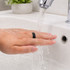 A black carbon fibre NFC ring is being rinsed under running water in a sink. 