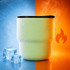 A double wall stainless steel round bottom camping mug in light green with a lid, surrounded by ice cubes and steam.