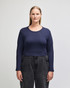 A long-sleeved, fitted crop top in navy blue, paired with high-waisted dark jeans. The top features a round neckline and has a logo.