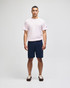 A man stands wearing a pink t-shirt and navy cotton gym shorts, featuring a logo on the shorts.