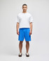 A model stands wearing blue cotton gym shorts and a white t-shirt, featuring a logo on the shirt.