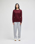 A long-sleeve t-shirt in maroon worn with grey sweatpants. The t-shirt features a logo on the sleeve.