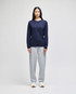 A long-sleeve navy T-shirt displayed on a model paired with grey sweatpants and white sneakers. The shirt features a logo.