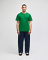 A green Champion adult jersey short sleeve t-shirt displayed on a model with navy blue trousers. The shirt features a logo.