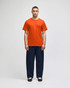 An orange short-sleeve t-shirt worn by a man, paired with navy blue pants, displaying a logo on the shirt.