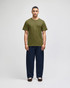 A model wearing an olive green short sleeve t-shirt and navy blue pants. The t-shirt features a logo.