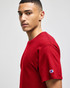 A man wearing a red Champion adult jersey short sleeve t-shirt, featuring a logo on the sleeve.