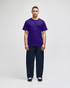 A model wearing a purple Champion adult jersey short sleeve t-shirt and dark blue pants, featuring a logo.