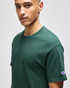 A green short sleeve T-shirt with a logo on the sleeve, modelled by a person against a neutral background.