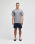 A model wearing a grey short sleeve t-shirt and navy shorts, featuring a logo on the t-shirt.