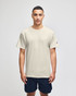 A light beige short sleeve t-shirt worn by a model, featuring a logo on the sleeve. Paired with navy shorts.