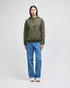 A model wearing an olive green pullover hooded sweatshirt with a logo, paired with blue jeans.