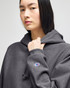 A dark grey pullover hooded sweatshirt with a logo on the sleeve, featuring a relaxed fit and drawstring hood.
