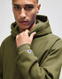 A man in a green hooded sweatshirt, featuring a logo on the sleeve and a focused expression.