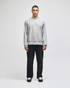 A grey crew sweatshirt worn by a model, paired with black trousers, featuring a subtle logo.