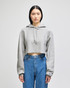 A grey cropped hoodie with a drawstring hood, featuring a logo on the sleeve, paired with blue jeans.
