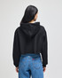A black cropped hoodie with a hood, worn by a person facing away, paired with blue jeans.