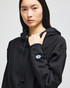 A black cropped hoodie with a hood, featuring a logo on the sleeve and a relaxed fit.